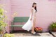 A woman in a white dress standing next to a green bench.