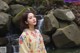 A woman standing in front of a waterfall wearing a kimono.