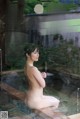 A naked woman sitting in a hot tub next to a waterfall.