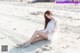 A woman in a white dress sitting on the beach.