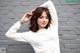 A woman in a white sweater posing in front of a brick wall.