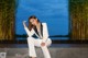 A woman in a white suit sitting on a wall.