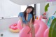 A woman in a bikini sitting on a pink inflatable pool float.